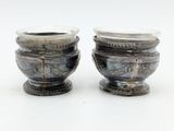 two silver vases sitting next to each other on a white surface