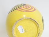 a yellow vase sitting on a white surface with a tag on it