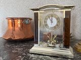 une horloge posée sur un comptoir, à côté d'une casserole en cuivre