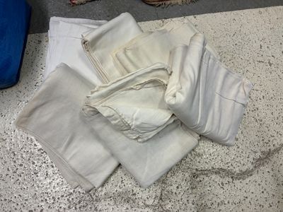 un tas de vêtements blancs par terre, à côté d'une valise bleue