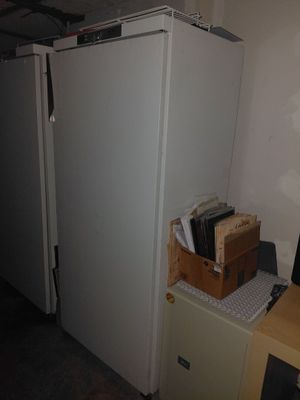 a white refrigerator in the corner of a room next to a desk
