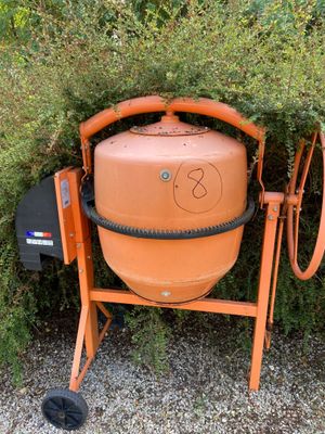 an orange cement mixer sitting in front of a bush