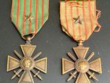 deux médailles et une croix posées sur une table, accompagnées d'un ruban rouge et vert