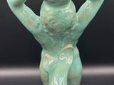 a green vase that has a woman holding a pot on it ' s head