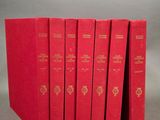 six livres rouges sont empilés les uns sur les autres sur une surface grise