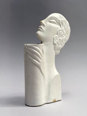 sculpture of a woman ' s head on a white vase on a gray background