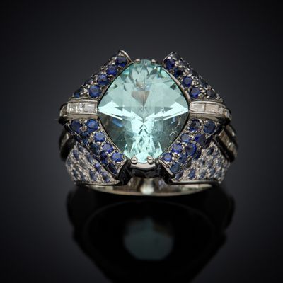 a close up of a ring with a large green stone surrounded by blue and white sapphires