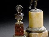 une statue représentant un homme debout sur un socle, à côté d'un buste d'homme