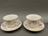 two cups and saucers with floral designs on them on a table