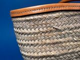 a wicker basket with a leather handle on a blue background