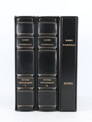 trois livres noirs ornés de lettres dorées, posés sur une surface blanche