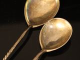 two silver spoons sitting on top of a table next to each other