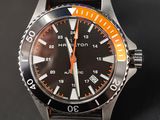 une montre noire avec une trotteuse orange sur fond noir