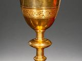 an ornate gold chalicee on a stand against a gray background