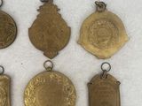 six antique brass medals are displayed in a row on a white surface