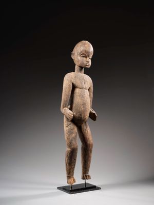 une statue en bois représentant un homme debout sur un socle noir