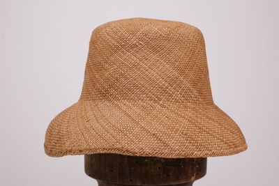 un chapeau de paille marron posé sur un support en bois, adossé à un mur blanc