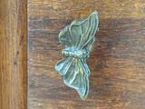 a metal butterfly that is on a wooden drawer