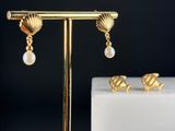 a pair of gold earrings with pearls and seashells on a stand