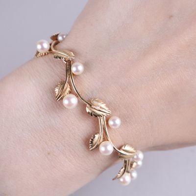 bracelet plaqué or orné de perles et de feuilles au poignet d'une femme