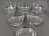 Six bols en verre transparent avec leurs couvercles sont posés sur une table.