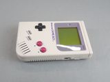 a white game boy sitting on a table with a green screen