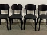 quatre chaises noires sont alignées contre un mur blanc