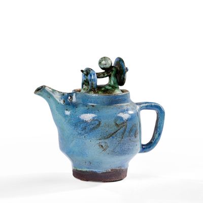 une théière bleue surmontée d'une petite figurine
