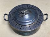 a metal pot with a bird on it on a table