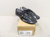 Des chaussures en cuir noir ornées de pompons sont posées sur une boîte