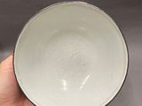 someone is holding a white bowl in their hand on a gray surface