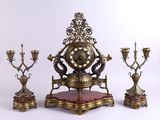 une horloge posée sur un socle sur lequel sont disposées trois bougies