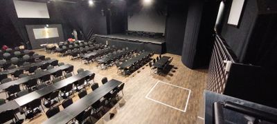 de nombreuses tables et chaises dans une grande salle équipée d'un écran de projection