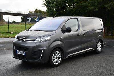 Une camionnette Citroën garée sur un parking, avec un pont en arrière-plan
