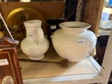 two white vases sitting on a shelf next to a clock