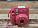 a pink camera on a wooden table with a red cord
