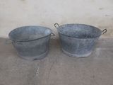 two metal buckets sitting next to each other on the ground