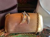 a gold purse with a wing on it sitting next to a purse