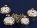 Trois montres de poche anciennes sont posées sur une table, reliées entre elles par une chaîne.