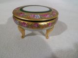 une boîte dorée et verte posée sur un socle, sur une surface blanche