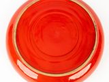 a red bowl with a gold rim sitting on a white surface