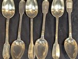 six cuillères en argent sont alignées sur une surface noire