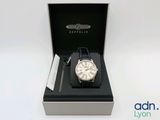 une photo d'une montre dans un coffret, posée sur une surface blanche
