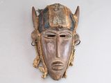 un vieux masque en bois accroché à un mur, orné de plumes