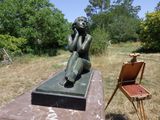 une statue représentant une femme assise sur un banc à côté d'une chaise