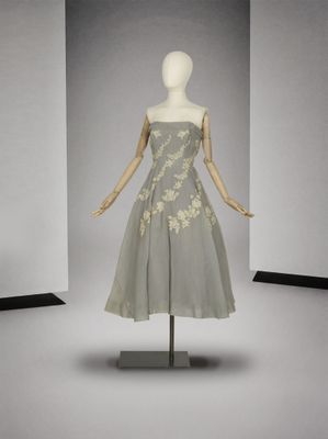 une photo d'un mannequin vêtu d'une robe grise, posé sur un socle