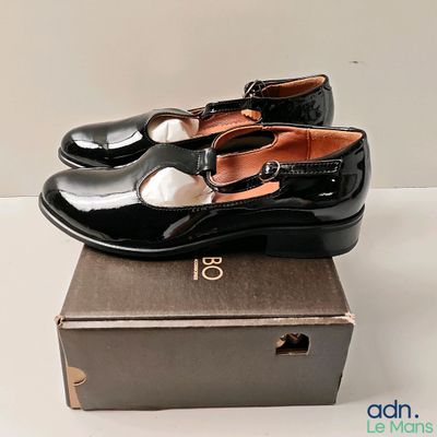 une paire de chaussures noires posée sur une boîte, elle-même posée sur une surface blanche
