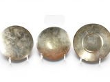 three silver dishes on stands on a white surface with a white background