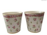 two cups with pink flowers are sitting side by side on a white surface