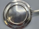 an antique silver plate with a spoon on a gray surface